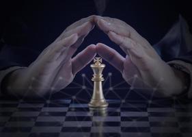 Hand of businessman protect the golden king chess to fighting silver king chess to play successfully in the competition with technology network background. Management or leadership strategy concept. photo