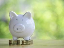 White piggy bank on gold coins stack 4 rows placed on a wooden table to save money invest for future. Concept for loan, property ladder, financial, real estate investment, taxes and bonus. photo