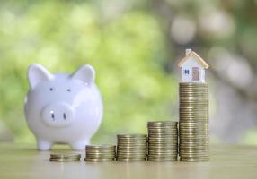 Coins stack 4 rows of gold coins and a white piggy bank placed on a wooden table to save money invest for future. Concept for loan, property ladder, financial, real estate investment, taxes and bonus. photo