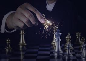 Hand businessman moving the golden knight chess fighting silver knight with fire sparks chess on chess board to successfully in the competition. Management or leadership strategy and teamwork concept. photo