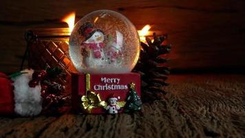albero di natale, giocattolo di babbo natale e pupazzo di neve nel globo di neve con candele accese per il nuovo anno o le vacanze di natale internazionali su sfondo di legno video