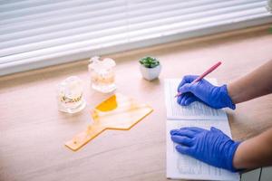 Dentist's hands in surgical gloves fill a paper card of a patient. photo