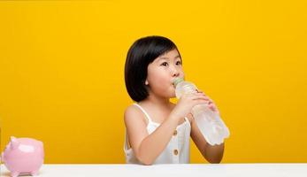 Beautiful young Asian woman drinking a glass of water at home. in a white table on a yellow background photo