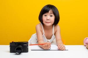 lindas fotos de chicas asia escribe un libro en la oficina para niños trabajadores. niños inteligentes. mesa blanca sobre un fondo amarillo.