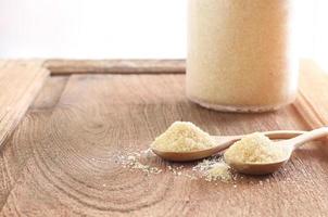 Two spoons of brown sugar and a bottle on wooden table against soft blur background  -  Selective focus photo