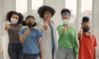 médico afroamericano y niños con máscara feliz pulgar arriba dedo en el hospital o clínica. foto