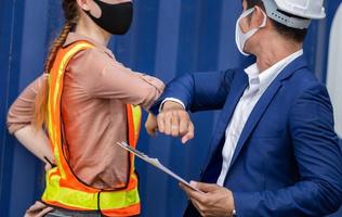 Industrial engineer and inspector colleagues wearing protective face masks greeting bumping elbows, Factory workers greeting each others with elbows during corona virus pandemic. photo
