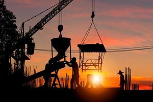Silhouette of Foreman and worker team at construction site with blurred sunset sky background photo