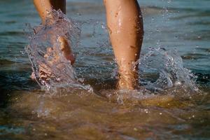 piernas de la niña caminando entre las pequeñas olas del mar. piernas de una niña corriendo hacia el océano en una playa de arena. piernas de niña de primer plano en aguas poco profundas. foto