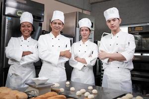 A Group of multiracial professional happy chefs team staff in white cooking uniforms stands in a row, arms crossed with confidence, cheerful smiles with commercial culinary jobs in restaurant kitchen. photo