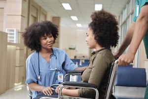 Young African American female doctor with stethoscope in uniform checks injury patient girl in wheelchair at outpatient accident clinic hospital, illness medical clinic examination, healthcare hall. photo
