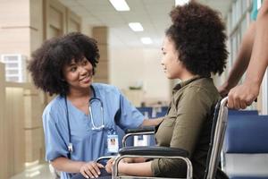 Young African American female doctor with stethoscope in uniform checks injury patient girl in wheelchair at outpatient accident clinic hospital, illness medical clinic examination, healthcare hall. photo