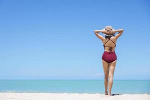 mujeres jóvenes en bikini y sombrero de paja se paran en una playa tropical disfrutando de la vista del océano de la playa en un caluroso día de verano. mar azul de fondo. khao lak, phang nga, tailandia. concepto de vacaciones de verano foto