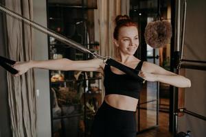 Joyful young woman pilates instructor doing hand strengh exercise on reformer photo