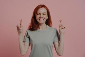 Hopeful red-haired female student crossing fingers with superstitious facial expression photo
