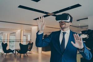 Businessman in futuristic VR headset touches air with his palms immersed in virtual reality photo