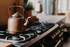 Hervidor de agua de aluminio viejo hirviendo en estufa de gas en la cocina contra un acogedor fondo borroso. Objeto antiguo fabricado en metal cobre. estilo vintage foto