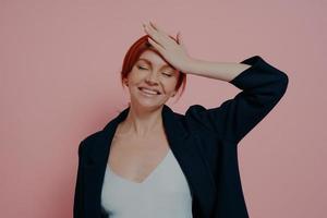 Beautiful laughing carefree red-haired woman isolated on pink studio background keeping hand on forehead photo