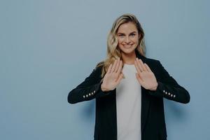 mujer joven sonriente y educada vestida con un blazer negro sobre una camiseta blanca manteniendo las manos en gesto de parada foto