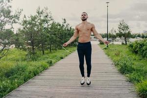 el hombre musculoso deportivo usa la cuerda para saltar para el entrenamiento cardiovascular al aire libre, tiene un cuerpo perfecto, respira aire fresco y demuestra resistencia, desarrolla el autodesarrollo. chico atleta con equipamiento deportivo foto