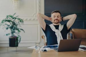 Young businessman watching video on laptop and feeling relaxed while working from home photo