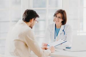 Woman doctor with stethoscope holds binder with patient personal medical card, consults patient who has medical problems, sit at hospital office, discuss medical checkup results, offers insurance photo