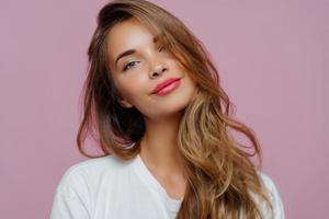 retrato de una joven modelo satisfecha y relajada inclina la cabeza, tiene maquillaje, cabello rubio, vestido con ropa blanca, posa contra un fondo morado, tiene una tez bien cuidada. gente, belleza, cuidado de la cara foto