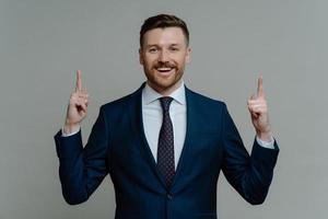 Happy businessman in suit pointing up with fingers and smiling at camera photo