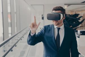 Smiling business professional in suit wearing VR headset on head using virtual reality at workplace photo