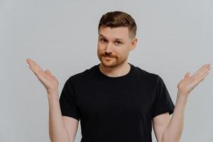 Isolated shot of confused young guy spreading hands sideways and feeling doubt while making choice photo