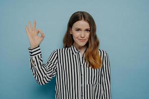 Confident smiling young girl in stripy blouse showing okay sign photo