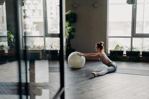 Sportive woman stretching legs in split position, training with large exercise ball photo