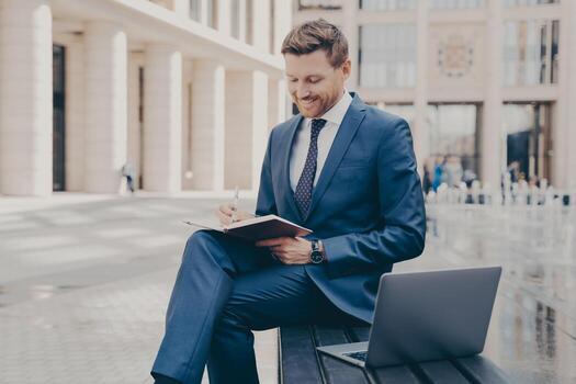 Successful business owner writing down information in notebook while working outdoors on weekend photo