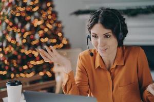 consultora de callcenter en auriculares hablando con el cliente mientras trabaja durante las vacaciones de navidad foto