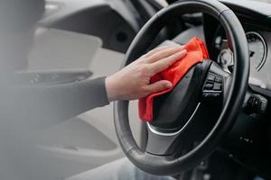 Close up of steering wheel inside of car and mans hand with cloth. Cleaning auto interior. Automobile detailing service. photo