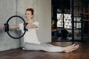 Young focused redhead woman doing strength exercises with pilates ring photo