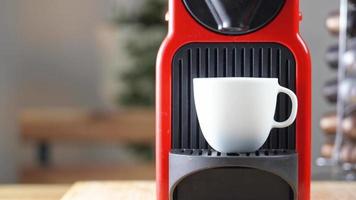 4k-Video, automatische Kaffeemaschine mit schwarzen Kaffeekapseln oder Kaffeepads, die Espressogetränk in eine weiße Keramiktasse mit heißem Rauch gießen. Frühstückszeit mit frischem Americano-Getränk.