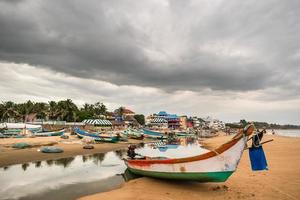 A fishing boat idles beside the tidal waters on the Mahabalipuram beach on a cloudy day.
