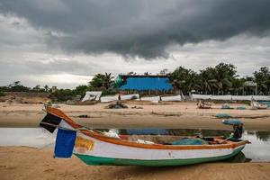 A fishing boat idles beside the tidal waters on the Mahabalipuram beach on a cloudy day. photo