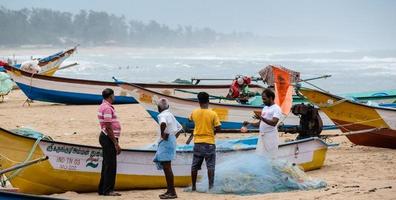 mamallapuram, tamil nadu, india - agosto de 2018, los pescadores trabajan en sus redes de pesca junto a sus botes en la playa de mahabalipuram. foto