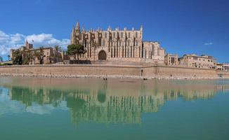 Famous medieval La Seu Cathedral reflecting in canal water against blue sky photo