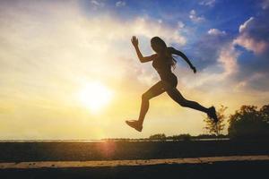 Silhouette of young woman running sprinting on road. Fit runner fitness runner during outdoor workout with sunset background. photo