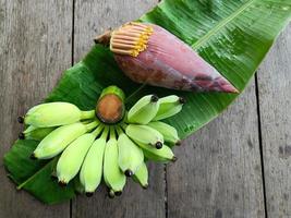 Green bananas and flower on banana leaves and brown wooden table photo