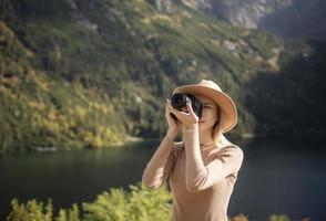 Photographer tourist traveler standing on green top on mountain holding in hands digital photo camera