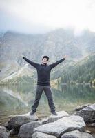 Young tourist man in a cap with hands up on the top of the mountains photo