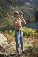Photographer tourist traveler standing on green top on mountain holding in hands digital photo camera