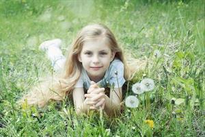 Image of pretty little girl lying down on dandelions field photo