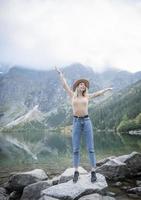joven turista en un sombrero con las manos arriba en la cima de las montañas foto