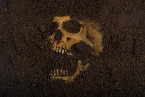 Beside of human skull buried in the soil concept of death and Halloween photo