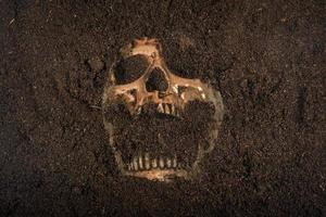 Beside of human skull buried in the soil concept of death and Halloween photo